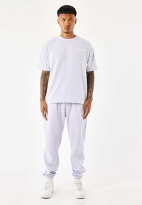 Conjunto de ropa deportiva de color púrpura claro, que incluye una camiseta de corte relajado con cuello redondo y pantalones jogger a juego con puños elásticos.