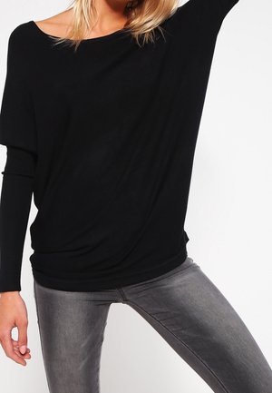 Black, loose-fitting top with a wide neckline and long sleeves, paired with fitted gray jeans; texture appears soft and slightly draped.