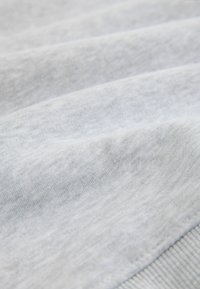 Jasnoszara bluza z miękką teksturą, z poziomymi fałdami i prążkowanym obszyciem dolnym. Tkanina wydaje się gładka ze subtelnym połyskiem.