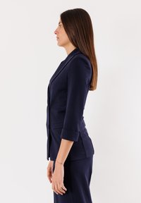 Blazer su misura blu navy con maniche a tre quarti, dotato di una vestibilità slim, spalle strutturate e tasche laterali. Tessuto con texture liscia.