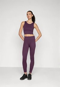 Lila sportos crop top és magas derekú leggings rugalmas anyagból, sima textúrával és testhezálló kialakítással. Fekete sportcipők.