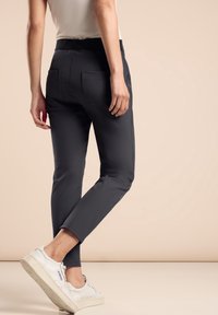 Smal passform mörkgrå byxor med en texturerad midjeband och två bakfickor, kombinerat med vita sneakers i en neutral miljö.