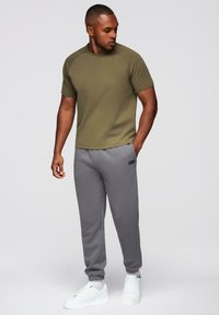 Olivengrønt kortærmet t-shirt, grå sweatpants, hvide sneakers. Tøjet har et tætsiddende design med ribbede detaljer og opkrøllede bukseben.