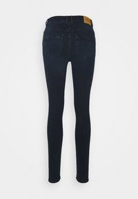 Jeans skinny azul-escuros com uma textura de denim suave, apresentando uma cintura alta, cinco bolsos e uma etiqueta de marca em couro castanho na parte de trás.