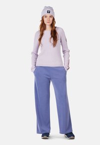 Helllila, geripptes Strickoberteil mit langen, enganliegenden Ärmeln. Lockere, hellblaue Jogginghose; graue und blaue Sportschuhe; lavendelfarbene Mütze mit Logo.