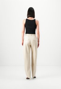 Top in jersey nero a coste, pantaloni beige a vita alta con tasche posteriori, texture liscia, fit dritto, e sandali con tacco sottile.