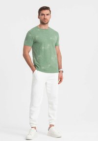 Vihreä, teksturoitu t-paita lyhyillä hihoilla yhdistettynä valkoisiin collegehousuihin ja rentoihin valkoisiin lenkkareihin. Yksinkertainen, nykyaikainen muotoilu.