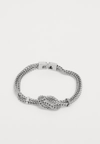 Bracelet en métal argenté avec un design tressé et un détail en nœud au centre, ainsi qu'une fermeture à crochet sécurisée. Maillons texturés tout au long.