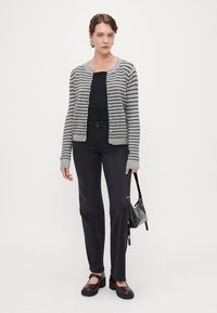 Grå og svart stripet cardigan, rund hals, knappelukking, brukt over en svart topp. Kombinert med mørke jeans og brune plattform sko.