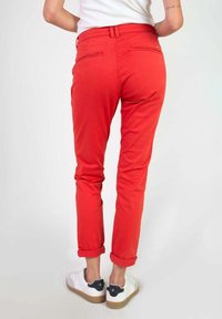 Pantalon slim rouge avec ourlets retroussés, doté de deux poches arrière et d'une texture lisse. Porté avec des baskets blanches et un haut simple.