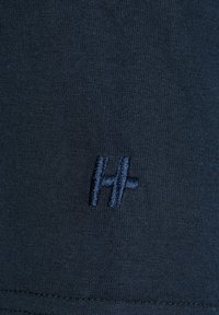 Marineblauwe stof met een gladde textuur, voorzien van een klein geborduurd logo in bijpassende kleur, gepositioneerd nabij de onderrand.