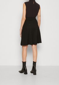 Černý top bez rukávů s vysokým výstřihem, kombinovaný s rozšířenou černou sukní a černými koženými kotníkovými botami. Hladká tkanina, minimalistický design.