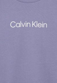 Lila crewneck sweatshirt tillverkad av mjuk bomullsmix, med vit "Calvin Klein" logotext över bröstet. Slät yta.
