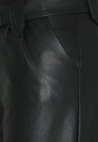 Lähikuva mustadest nahkpükstest, millel on nähtav õmblus ja kinnitatud vöökohaga nööp.