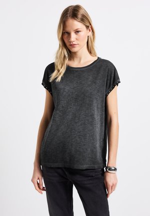 Camiseta negra de manga corta en una suave tela texturizada. Cuello redondo con acentos de tachuelas en las mangas. Corte holgado y diseño recto.