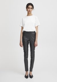 Pantalons en simili cuir noir au design élégant et ajusté, associés à un t-shirt en coton blanc uni et des ballerines noires pointues.