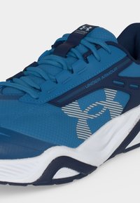 Μπλε αθλητικό παπούτσι τρεξίματος Under Armour με λευκή και ναυτική σόλα, ριγωτό λογότυπο στο πλάι και κορδόνια δεμένα από πάνω.