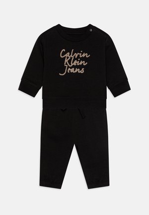 Mustast puuvillast kahe-osaline komplekt, mis sisaldab pika varrukaga topsi, millel on beež "Calvin Klein Jeans" logo, ja kokku sobivaid pükse kummitasku ning nööriga.