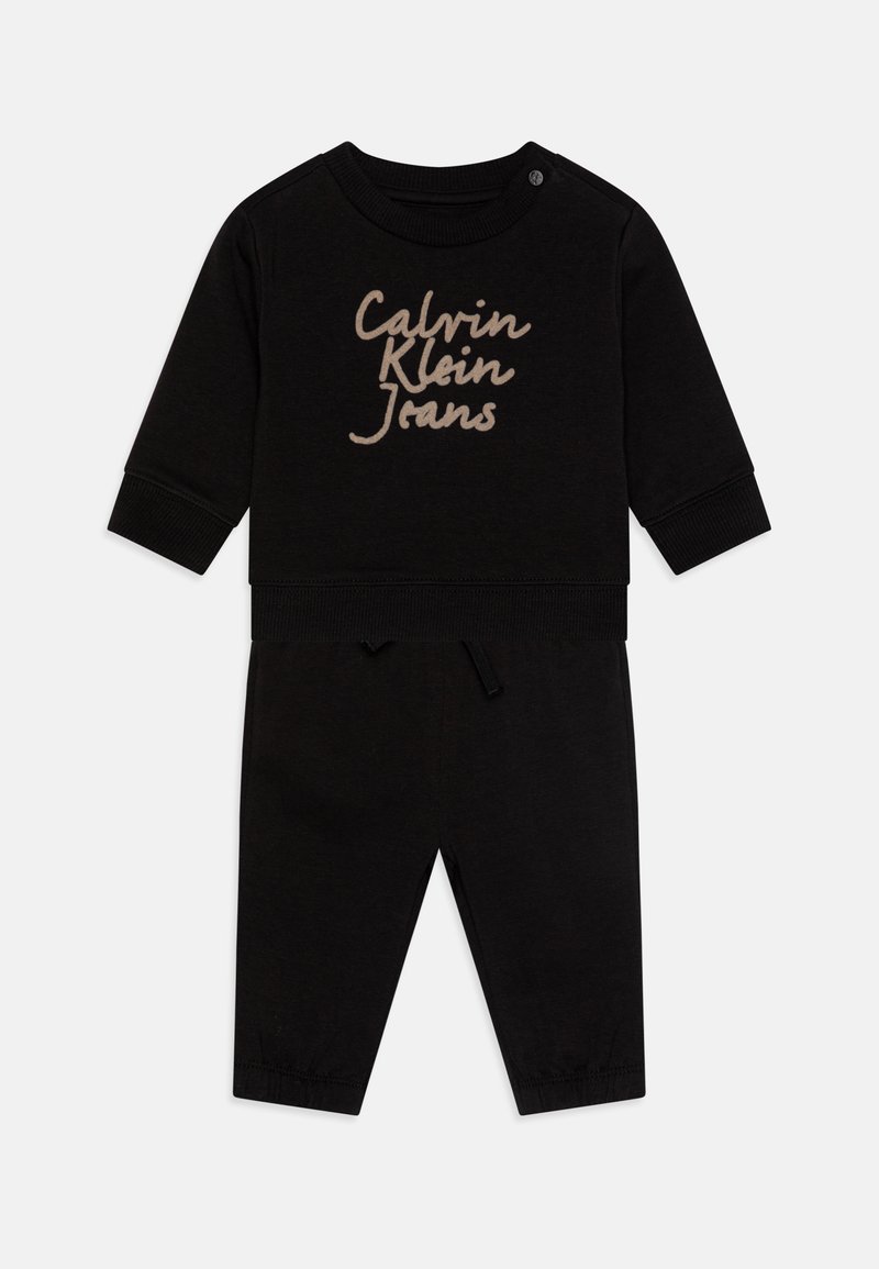 Mustast puuvillast kahe-osaline komplekt, mis sisaldab pika varrukaga topsi, millel on beež "Calvin Klein Jeans" logo, ja kokku sobivaid pükse kummitasku ning nööriga.