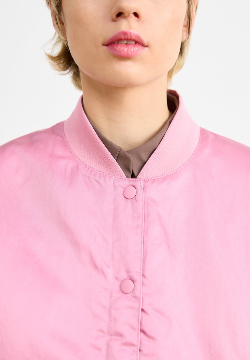 Rosa Bomberjacke mit Stehkragen, ausgestattet mit einer glatten, leicht glänzenden Textur und Knopfverschlüssen vorne.
