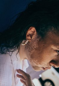 Cuff d'oreille en perles avec accent doré, comportant plusieurs perles blanches et un design texturé, porté par une personne aux cheveux ondulés et foncés.