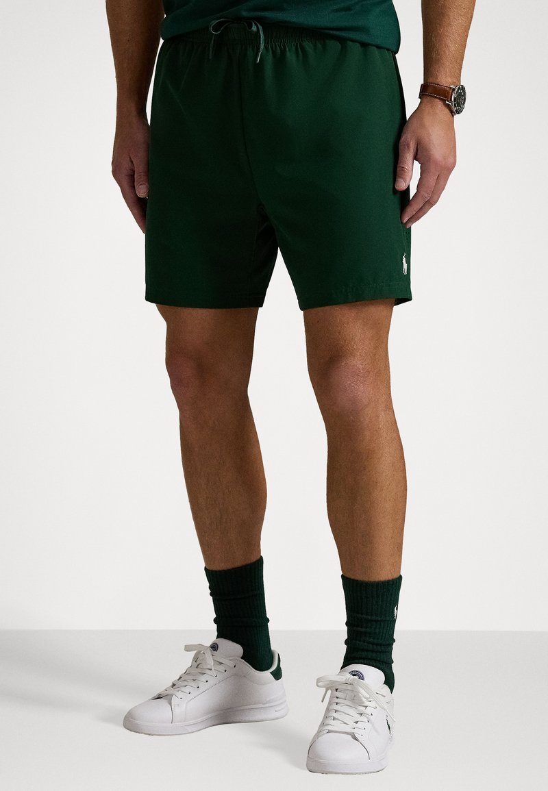 Pantaloni scurți sport verzi cu talie elastică și șnur. Prezintă un mic logo pe partea din dreapta jos. Purtați cu încălțăminte albă și șosete verzi.