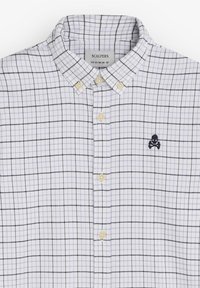 Camisa de cuadros blanca y marino con cuello abotonado, dos botones amarillos y un pequeño logotipo de calavera bordado en el pecho.