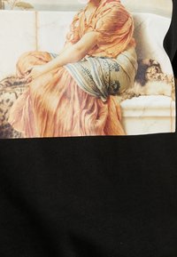 Black T-shirt featuring a detailed printed design of a woman in soft orange attire with a blue patterned sash, seated against a marble background.