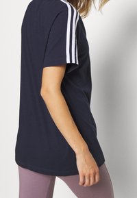 Camiseta de color azul marino de algodón con mangas cortas, que presenta tres rayas blancas en los hombros y un corte holgado, combinada con leggings rosas.