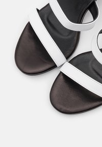 Des sandales noir et blanc avec deux larges brides, une texture en cuir lisse, un design à bout rond et une semelle plate.