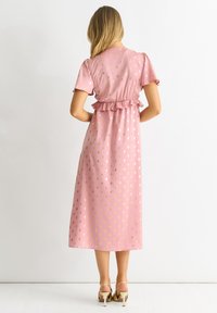 Pink midi dress with golden polka dots, short puffed sleeves, ruffled waist detail, and a flowing silhouette, paired with gold heels.
