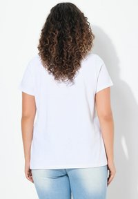 Camiseta blanca de manga corta con escote redondo, que presenta un corte holgado y una textura de algodón suave y lisa. Sin diseños ni patrones visibles.
