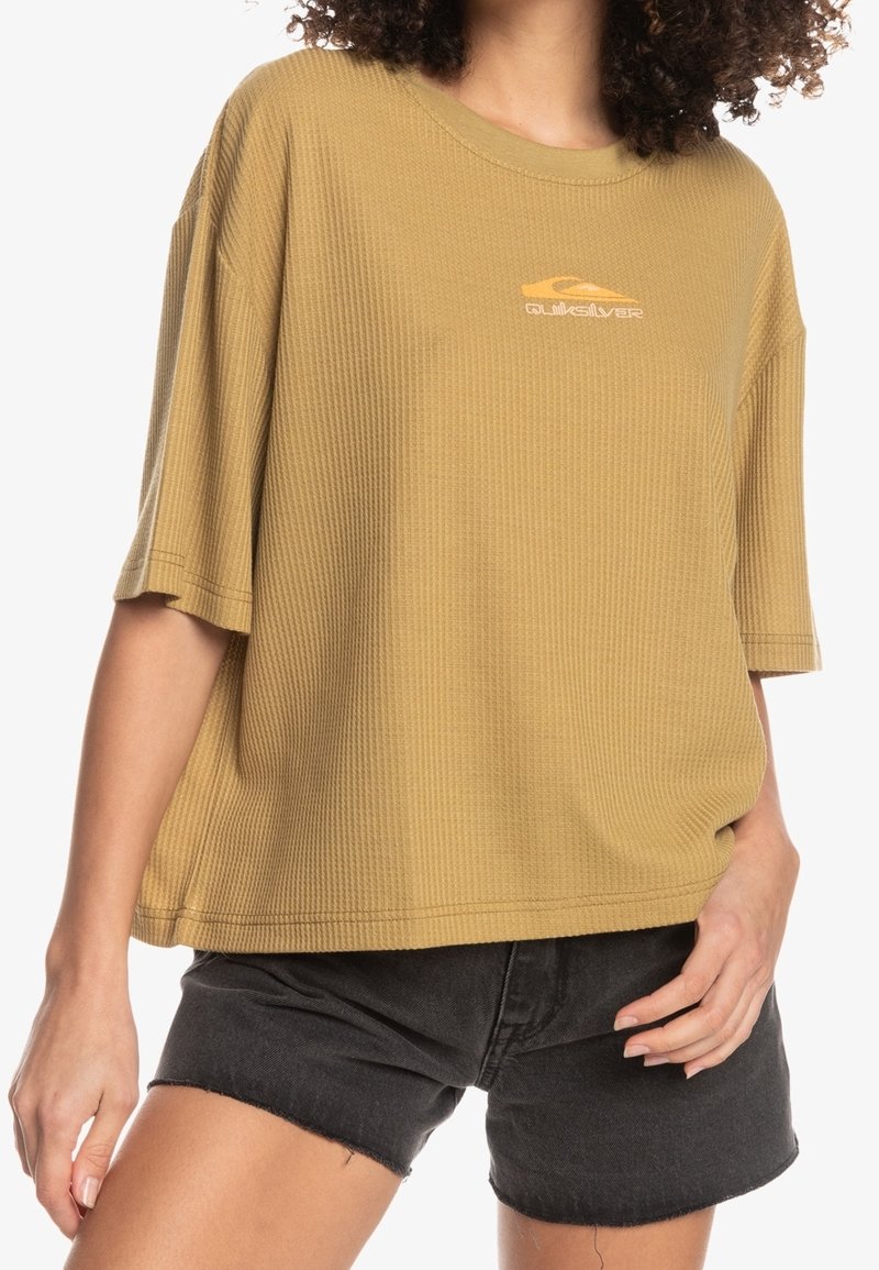 Olivgrön oversized T-shirt i texturerat tyg, med rund halsringning och korta ärmar, samt en liten orange logotyp på bröstet.
