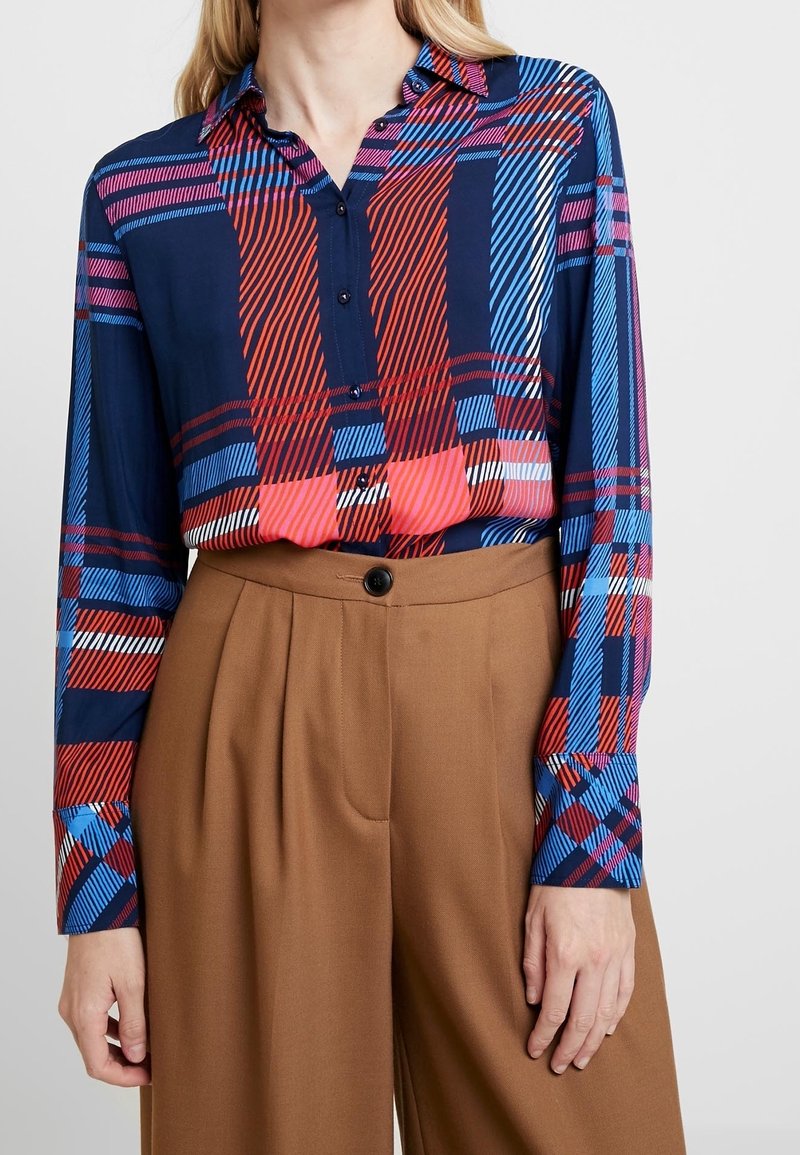 Námořnická košile na knoflíky s vícebarevným kostkovaným vzorem; dlouhé rukávy; ve spojení s hnědými kalhotami s vysokým pasem; hladká textilie.