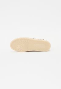Semelle de chaussure en caoutchouc beige avec un motif en chevrons texturé, comprenant de petites accents en relief. Fini lisse avec une section de talon arrondie.