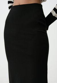 Zwarte, aansluitende rok van soepel, rekbaar materiaal. Hoge taille, enkellang met minimale details. Strakke silhouet en geen zichtbare sluitingen.