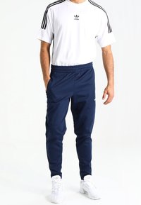 White t-shirt with black adidas logo and three stripes on sleeves, paired with navy elastic waistband joggers and white sneakers.