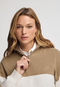 Suéter de cremallera bloqueado en color beis y blanco, hecho de un suave tejido de punto, con cuello, puños acanalados y un parche de logo en el pecho.