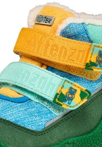 Scarpa per bambini multicolore con tomaia in denim blu, fasce gialle e verdi, e suola in gomma verde texture. Presenta un rivestimento fluffy e dettagli a forma di orsetto.