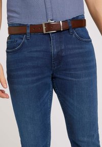 Dark blue denim jeans with a slim fit, five pockets, and a brown leather belt featuring a silver metal buckle. Smooth texture.