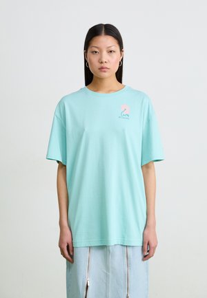 T-shirt en coton vert menthe avec des manches courtes, un col rond, et un petit design de logo rose sur la poitrine gauche.