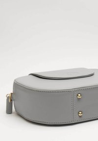 Borsa in pelle grigia con forma arrotondata. Presenta una chiusura a patta, dettagli in metallo dorato e cuciture lungo i bordi.