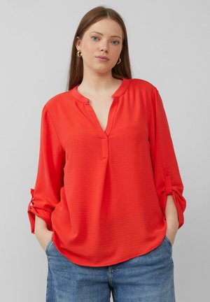 Red, lightweight blouse with a V-neck and roll-tab sleeves. Features a relaxed fit and subtle texture, paired with blue jeans.