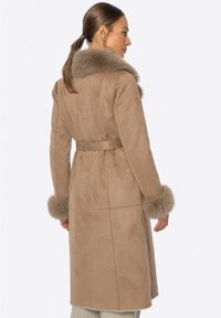 Abrigo de ante marrón con cuello y puños de piel, mangas largas, cintura ceñida con cinturón y corte recto, que presenta una textura suave y lisa.