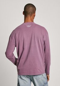 Long-sleeve purple cotton t-shirt featuring a crew neckline and a small white print at the back. Soft texture with a relaxed fit.