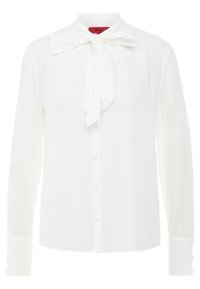 Blouse blanche à manches longues avec un col à nœud, une fermeture à boutons sur le devant et des accents en bouton sur les poignets. Fabriquée en tissu léger et texturé.