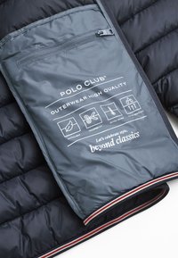 Granatowa pikowana odzież wierzchnia z szaro-zamkniętą kieszenią. Wyróżnia się logo oraz ikonami pielęgnacyjnymi. Zawiera czerwono-szare paski akcentujące na dole.