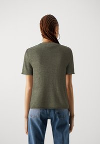 Olivgrüner, kurz�ärmliger Strickpullover mit strukturiertem Finish. Kombiniert mit hochgeschnittenen blauen Denim-Jeans, die eine lockere Passform und klassischen Stil zeigen.