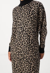 Leopardmönstrad klänning i beige och svart, med hög krage och långa ärmar. Tillverkad av mjukt stickat material med ribbade muddar.