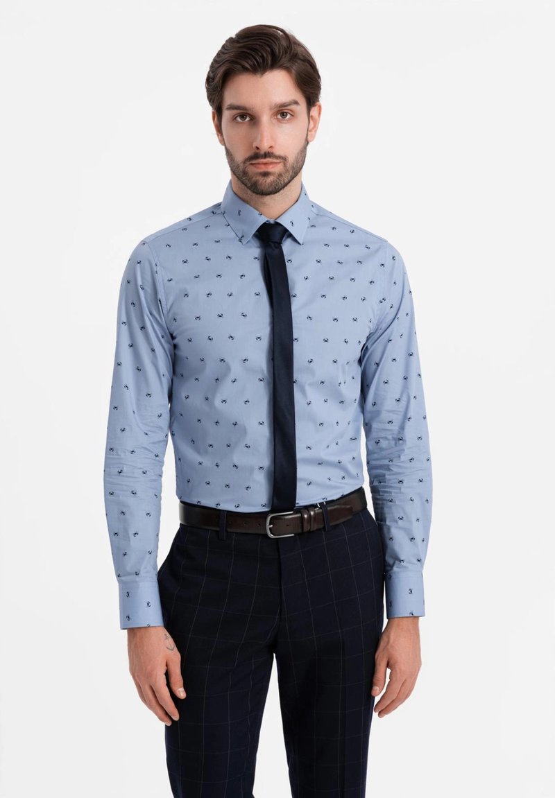 Camisa de manga larga azul claro con pequeños patrones en navy, combinada con una corbata oscura y pantalones cuadros en navy. Textura suave y diseño ajustado.